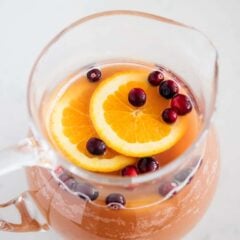 A glass pitcher with an easy holiday punch recipe garnished with orange slices and cranberries.