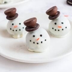 Snowman oreo balls coated in white chocolate and decorate with a Hershey's kiss hat, eyes, note and carrot.