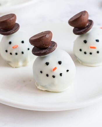 Snowman oreo balls coated in white chocolate and decorate with a Hershey's kiss hat, eyes, note and carrot.