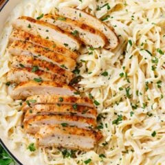 Chicken fettuccini alfredo with sliced chicken breast in a white pot.