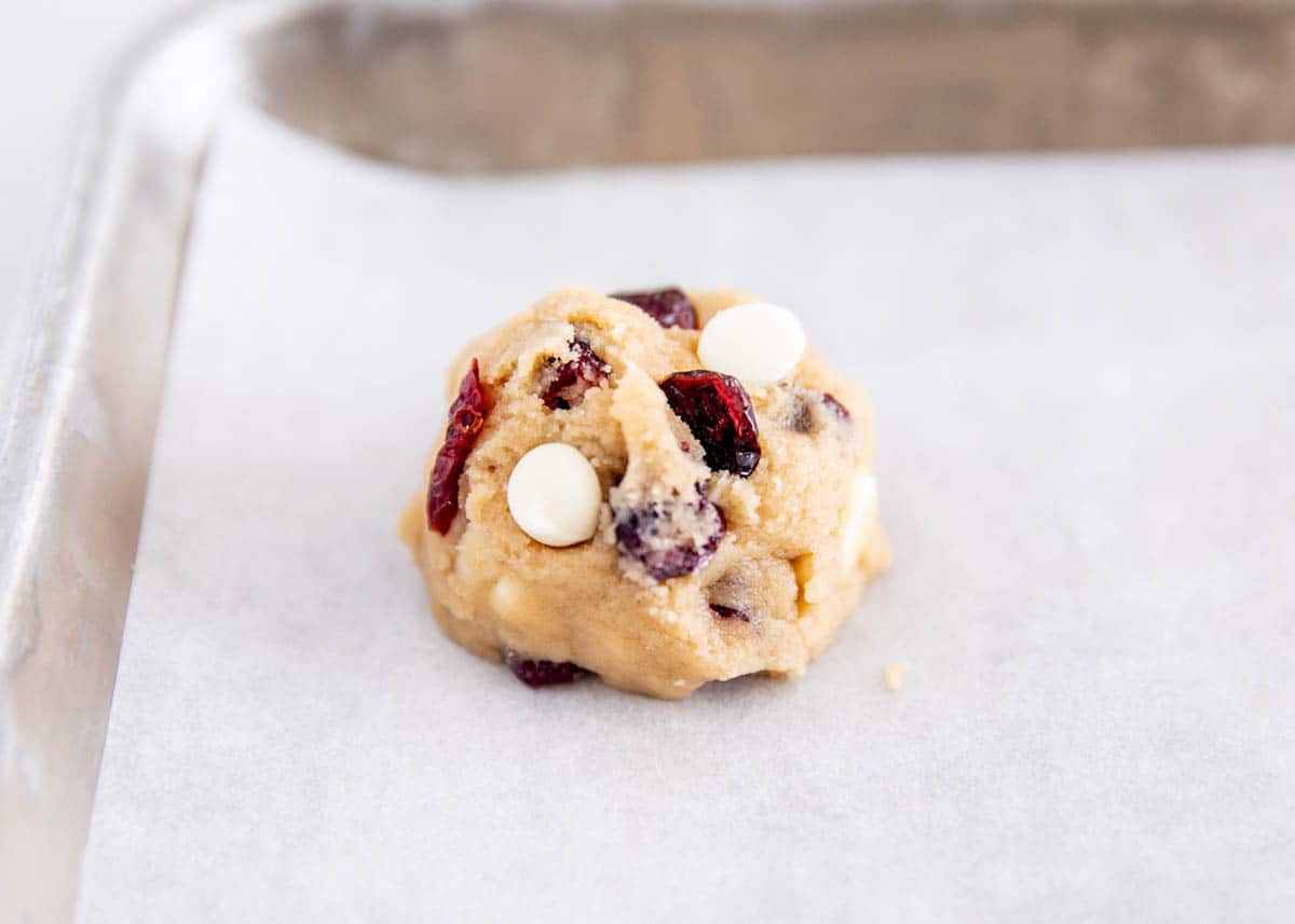 Scooped white chocolate cranberry cookie dough ready to bake on a parchment-lined baking sheet.