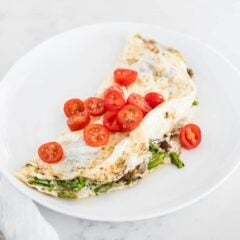 Fluffy egg white omelette topped with cherry tomatoes on a white plate.