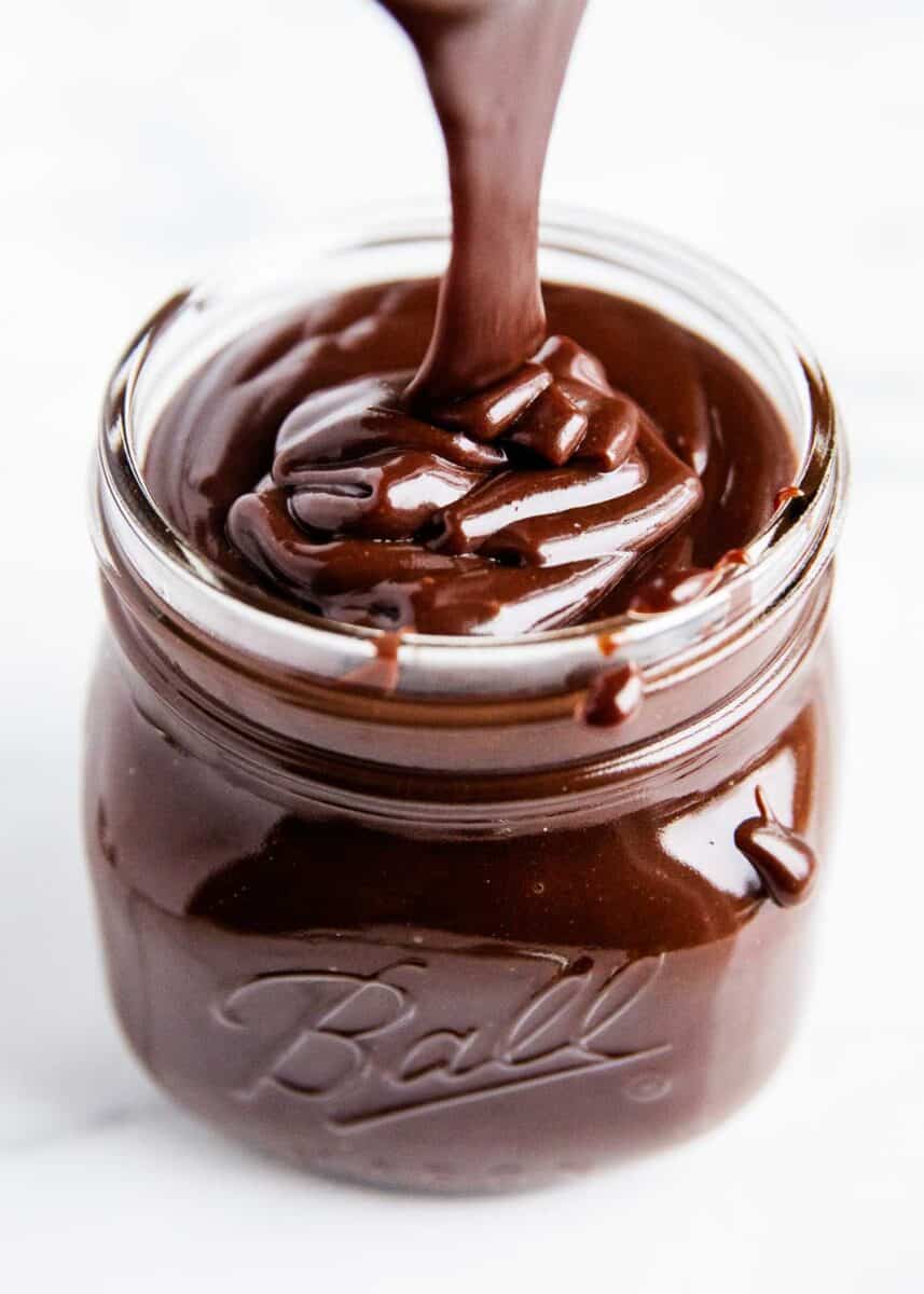 Pouring hot fudge sauce in a glass jar. 