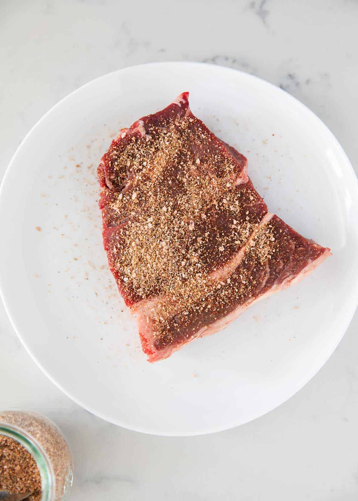 Steak with steak rub on white plate.