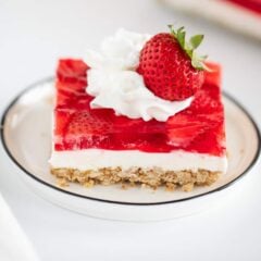 Strawberry pretzel salad on white plate garnished with whipped topping and a strawberry.