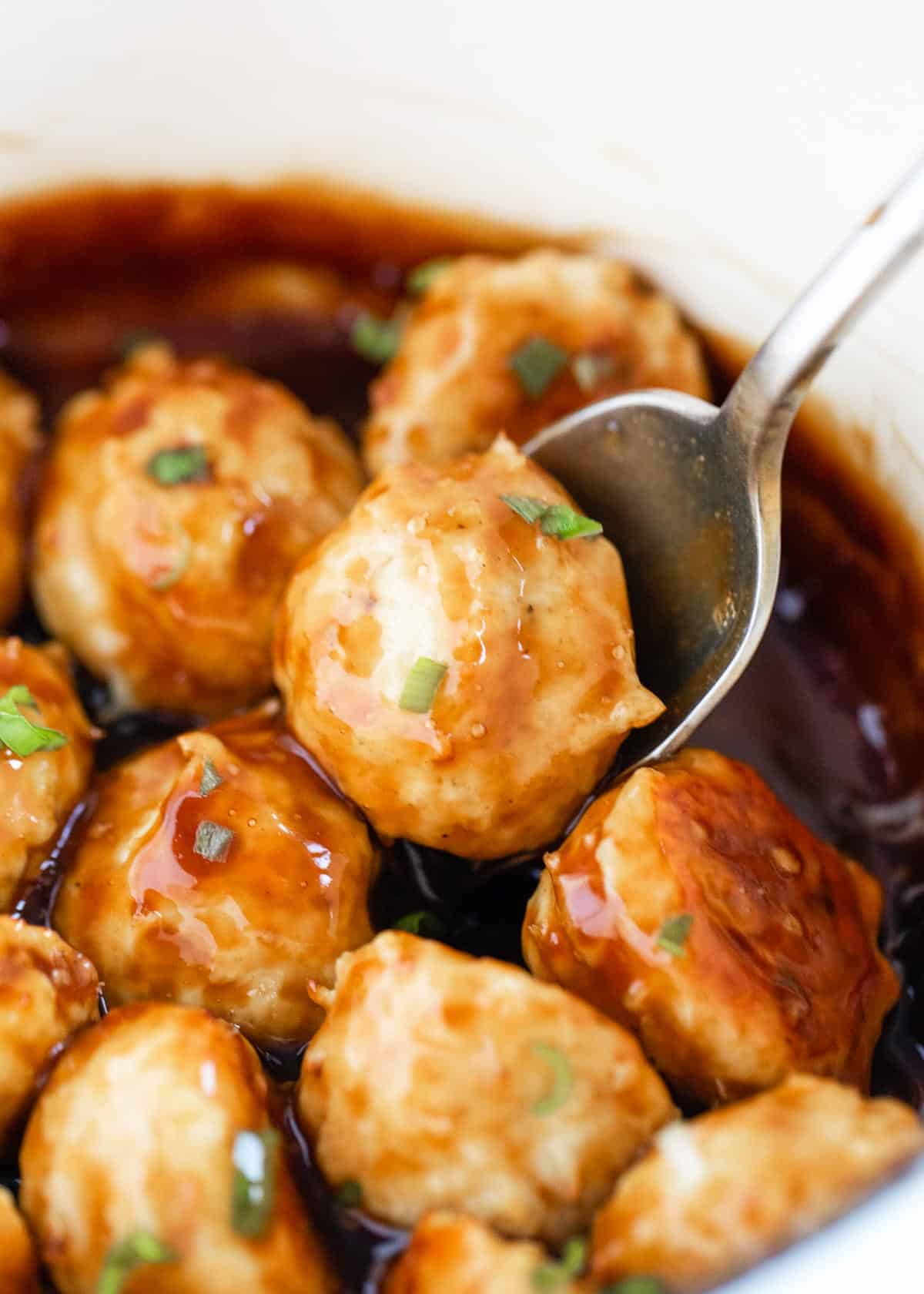 Meatballs in a sauce with a serving spoon. 
