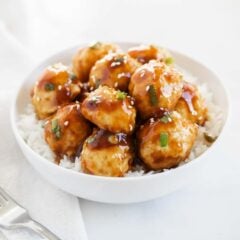 Teriyaki chicken meatballs in a white bowl with rice and garnished with sesame seeds.