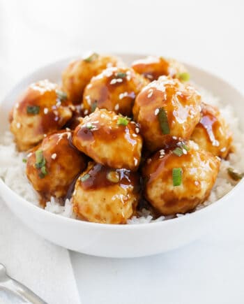 Teriyaki chicken meatballs in a white bowl with rice and garnished with sesame seeds.