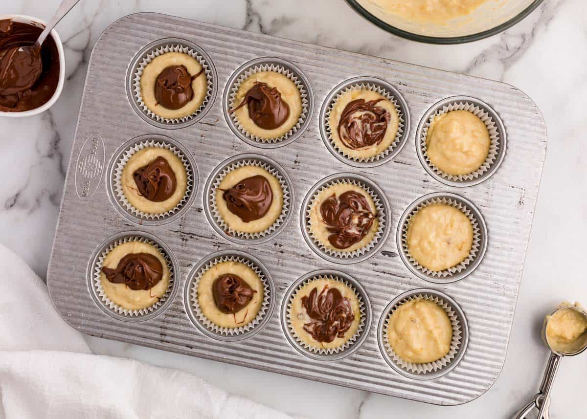 Banana muffins batter with a Nutella swirl in a muffin pan.