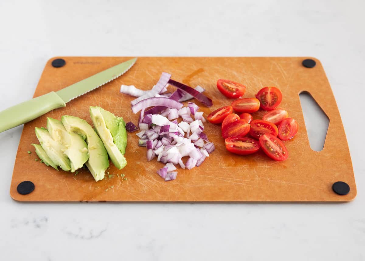 Chopped avocado, red onion and tomato on cutting board.