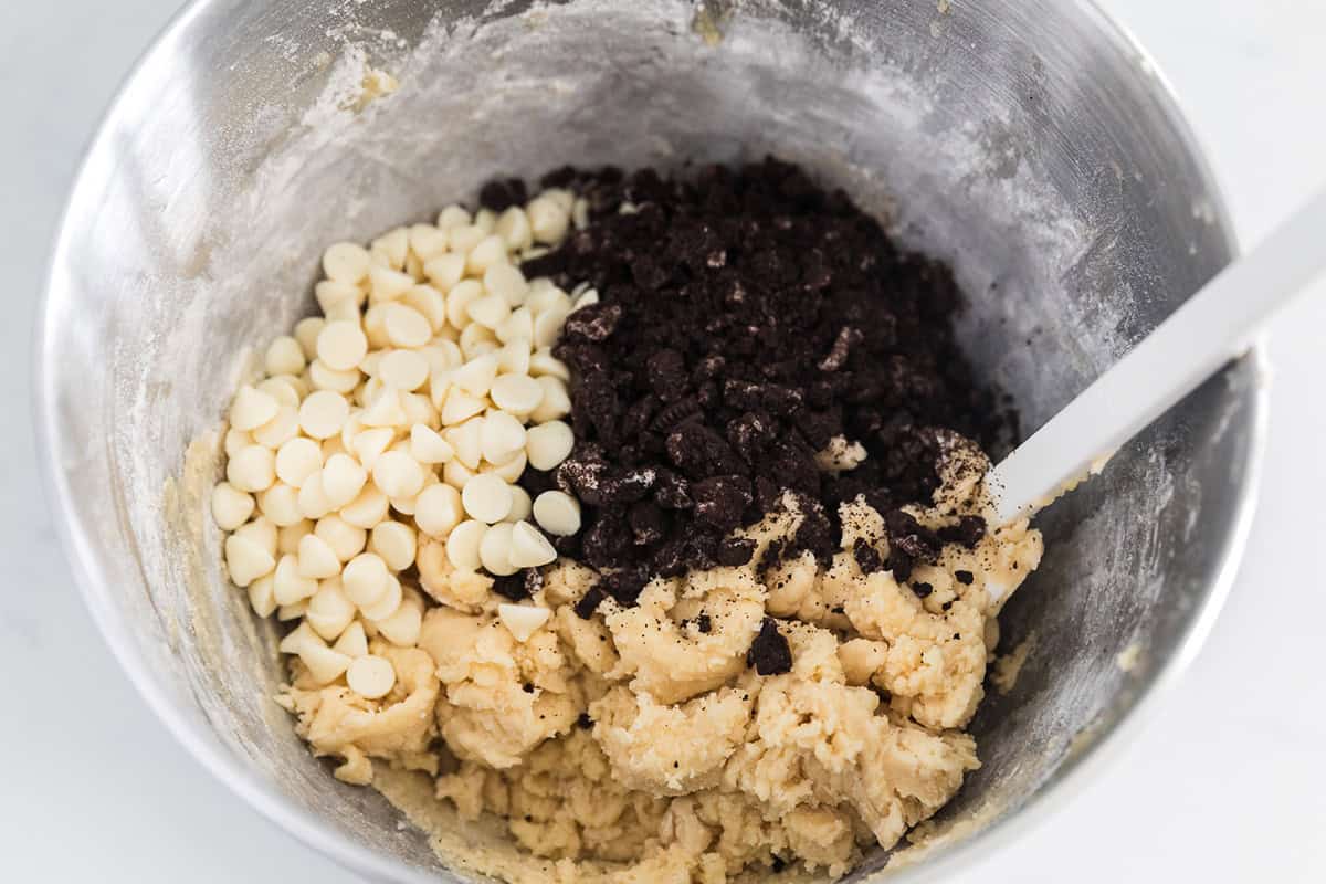 Cookie dough in a bowl with white chocolate chips and crushed Oreo pieces ready to be folded in.