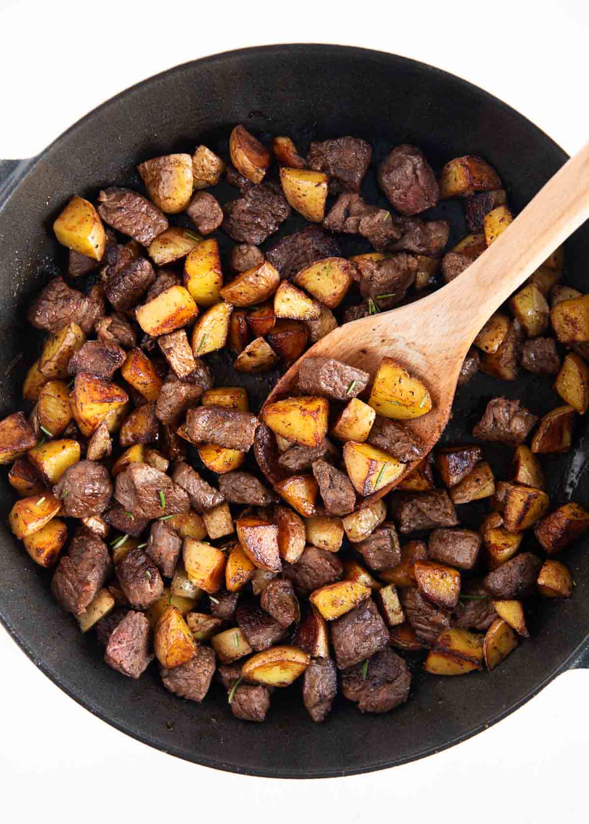 Steak bites and potatoes in a skillet.