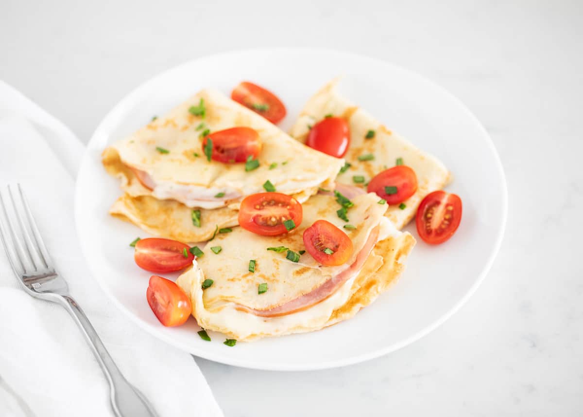 Ham and cheese crepe on white plate.