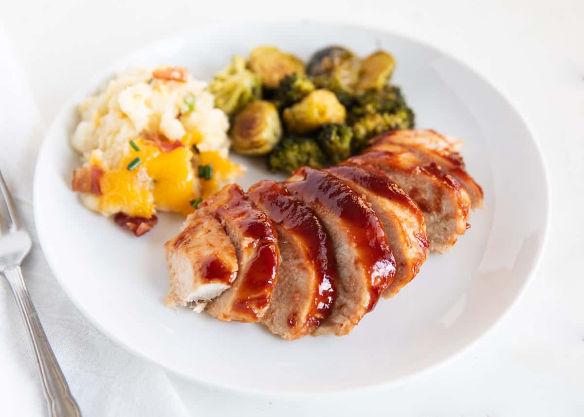 Juicy and tender baked chicken breast coated in a sweet and tangy BBQ glaze is an easy weeknight dinner that the whole family will love. This is a no fuss baked BBQ chicken recipe made with only 2 simple ingredients and 5 minutes of prep! Baked bbq chicken on white plate.