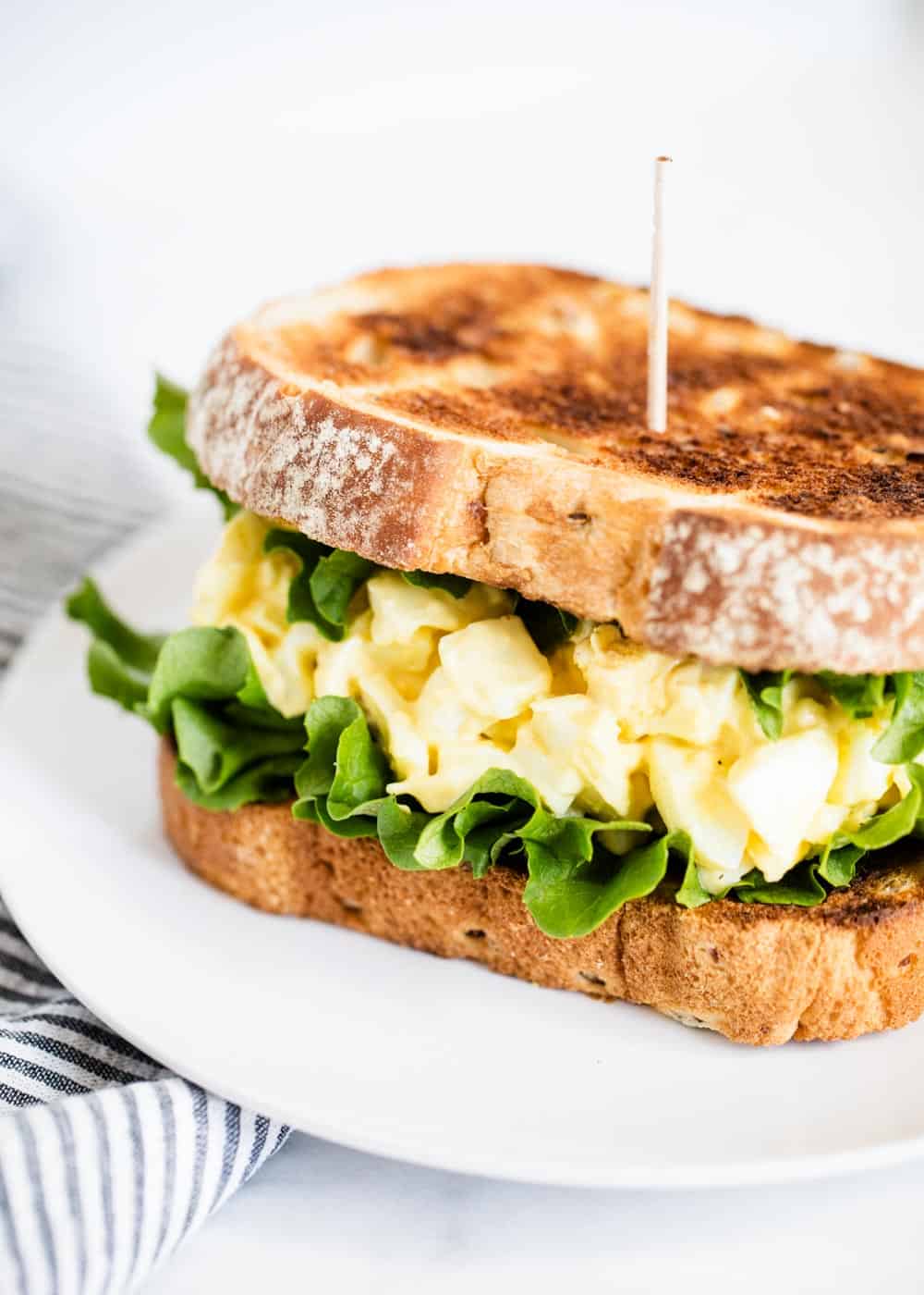 Egg salad sandwich on white plate.