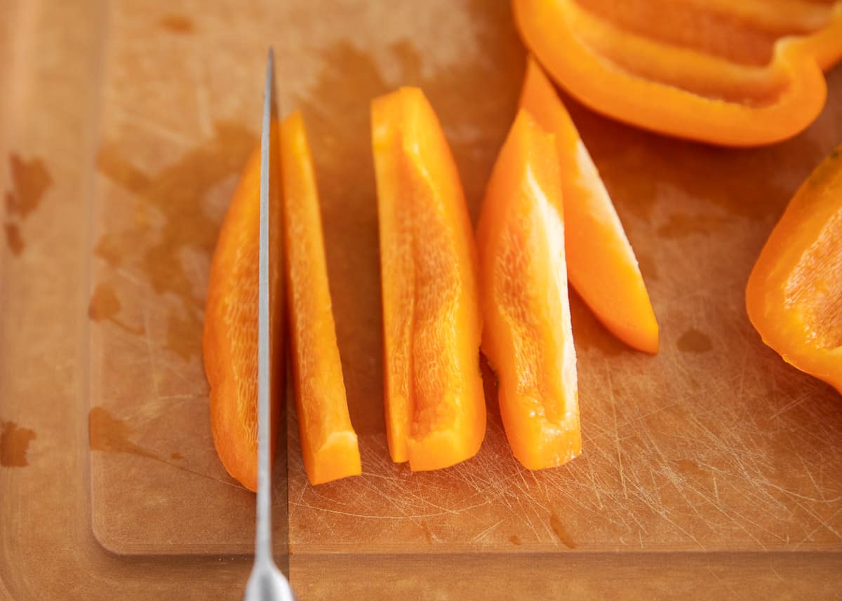 Orange bell pepper being cut on cutting board.