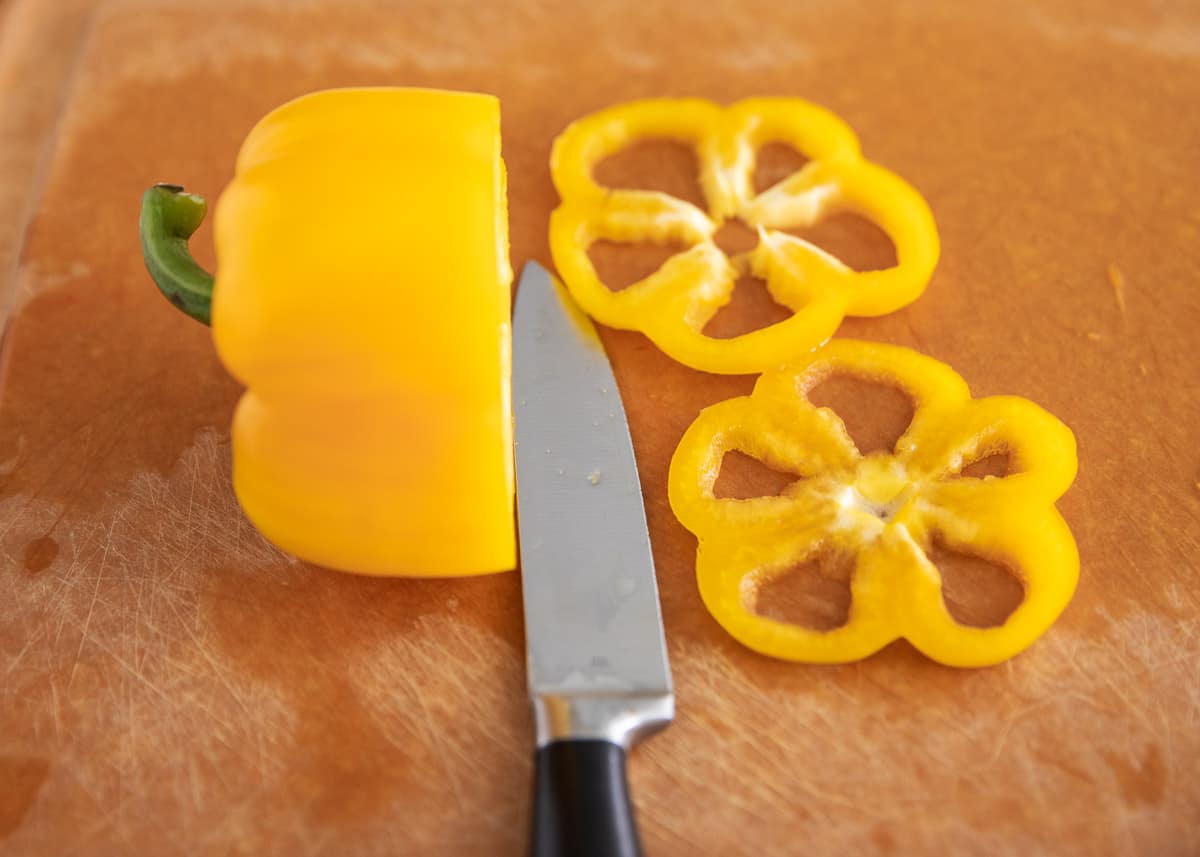 Yellow bell pepper being cut into rings on cutting board.