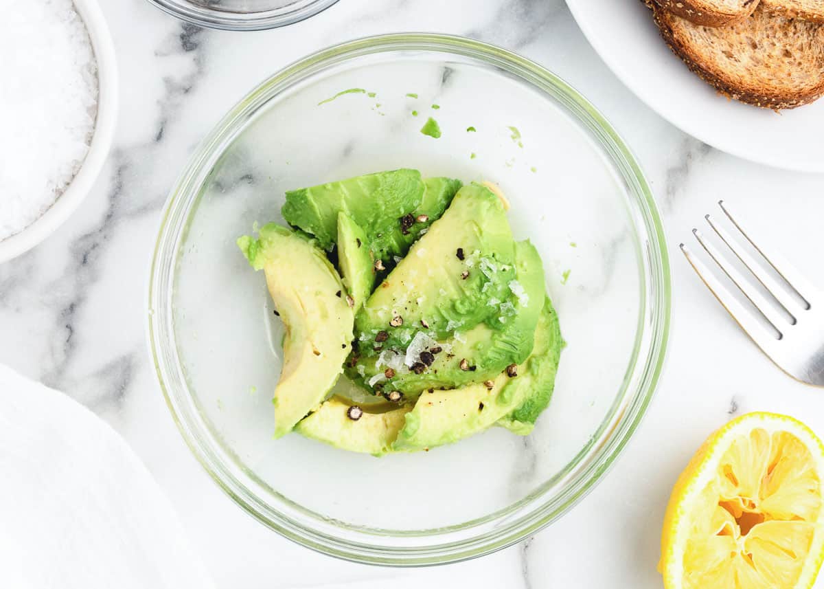 Mixing avocado in clear bowl.