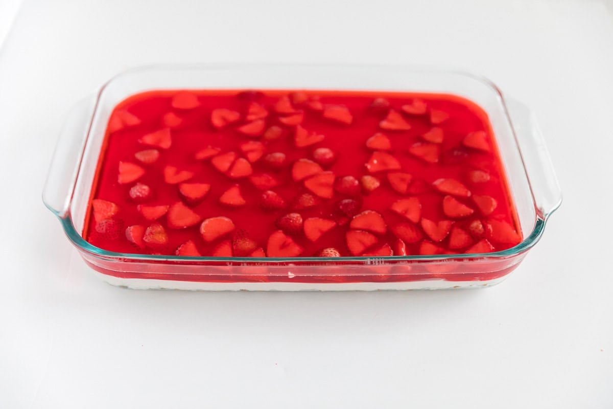Strawberry Jell-O and fresh strawberries poured over cream cheese layer in a glass baking dish.