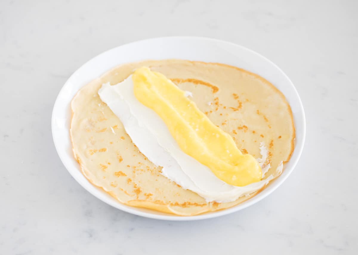 Assembling lemon crepes on white plate.