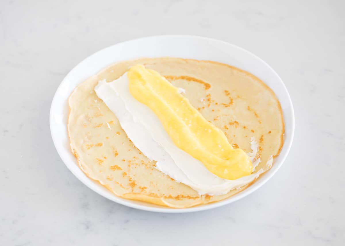 Assembling lemon crepes on white plate.