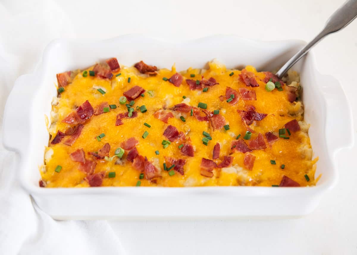 Loaded baked potato casserole in white baking dish with a serving spoon.