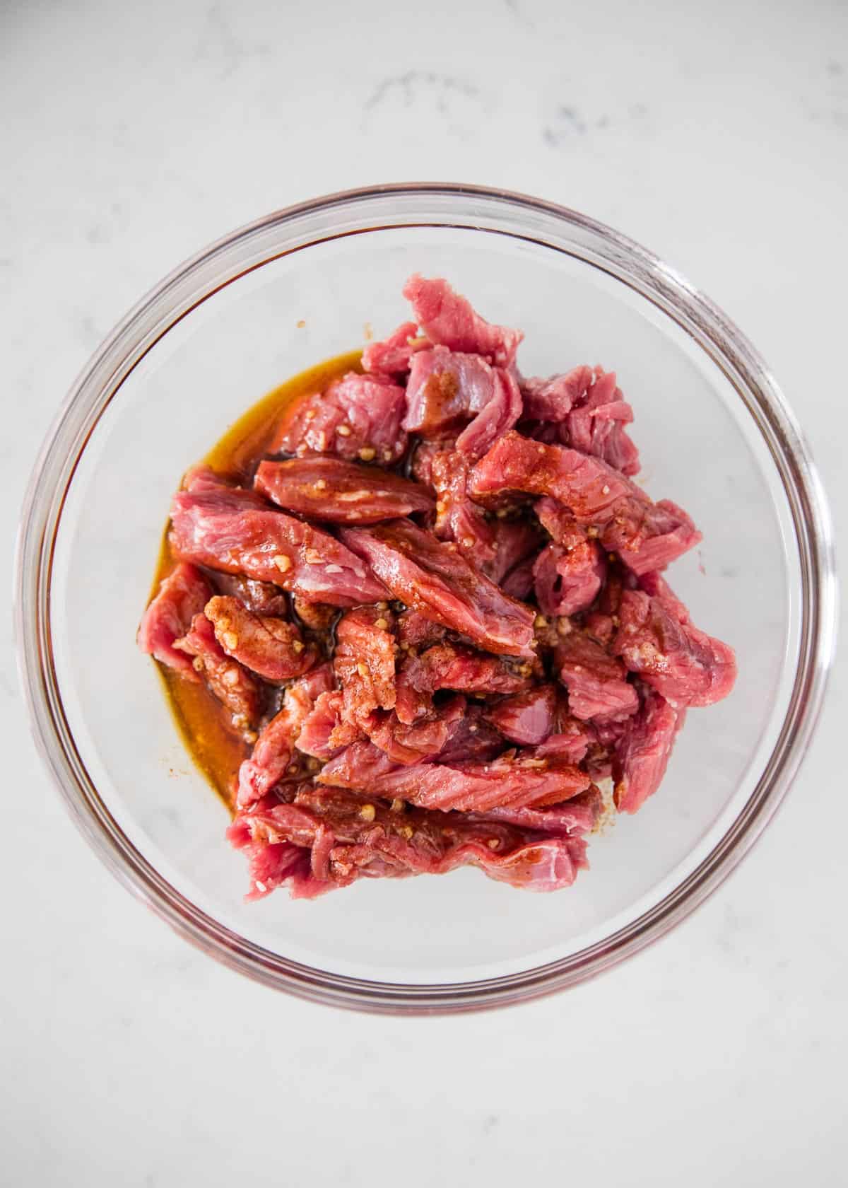 Steak being marinated in bowl.