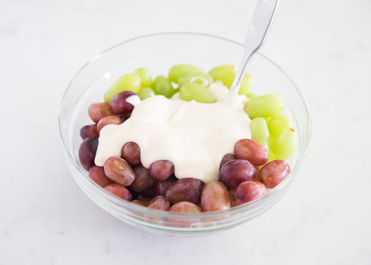 Grape salad ingredients in clear bowl.