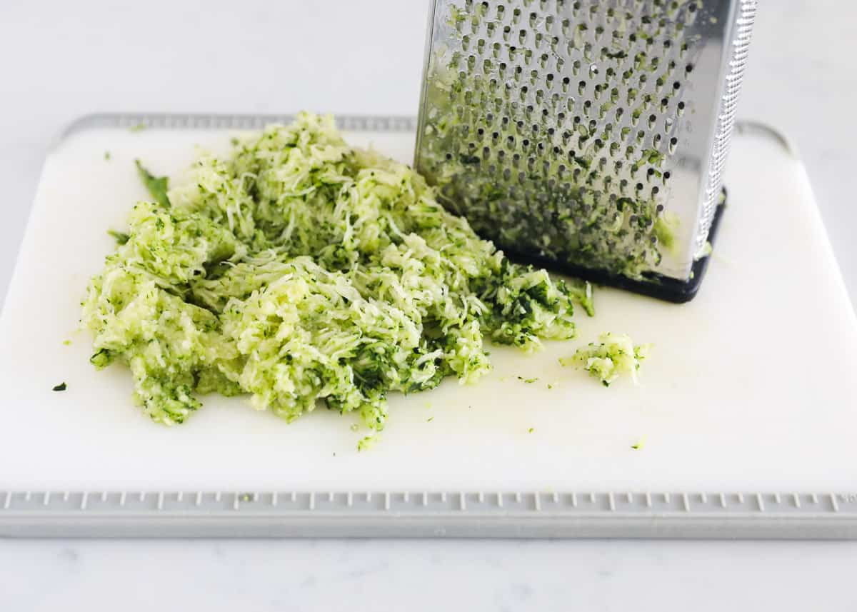Fresh zucchini being shredded on a box grater for muffin batter.
