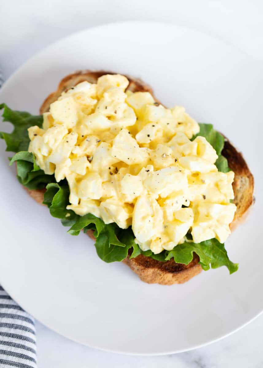 Open face egg salad sandwich on white plate.