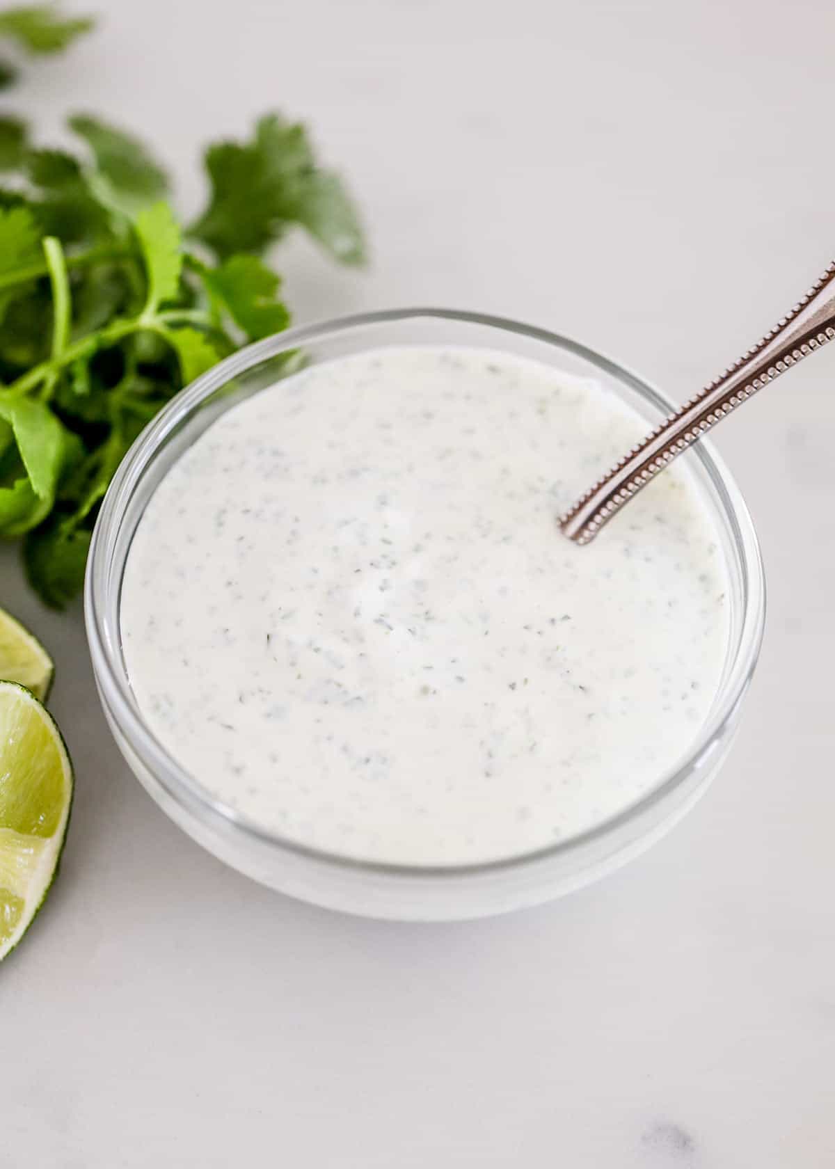 Make this refreshing, zesty cilantro lime crema made with 5 ingredients in 5 minutes, and use it to replace your everyday sour cream on everything from tacos, and burritos to salads and grilled veggies! Mexican crema in a glass bowl with a spoon in it.