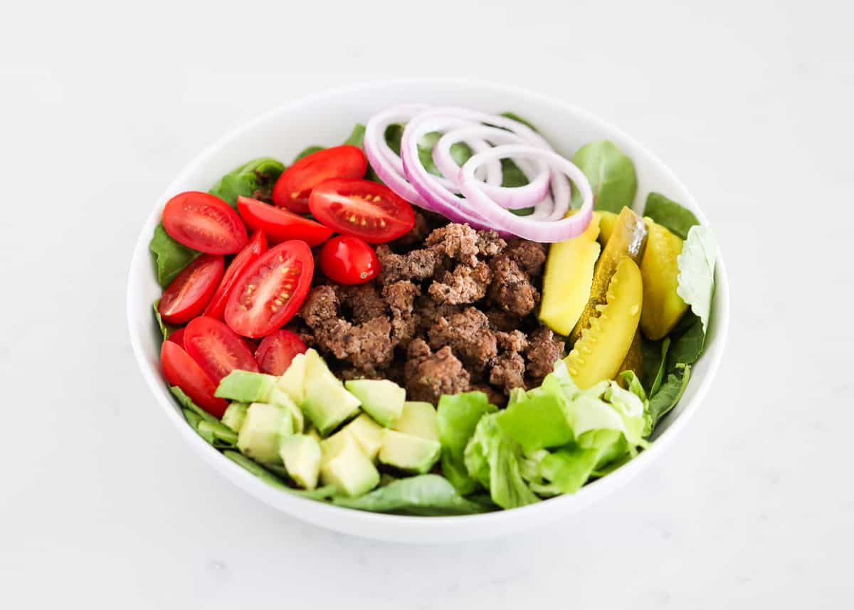 Burger salad ingredients in white bowl.