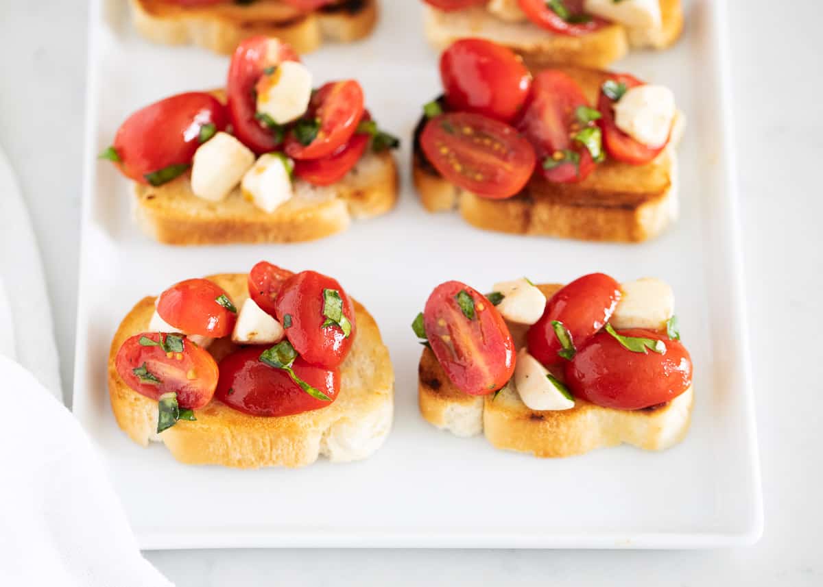 Bruschetta Caprese is a summer appetizer made with a slice of lightly toasted bread, fresh ripe tomatoes, basil, and good quality mozzarella tossed in a balsamic vinaigrette. It's a simple appetizer that comes together in minutes and is always a crowd favorite! Caprese bruschetta on plate.