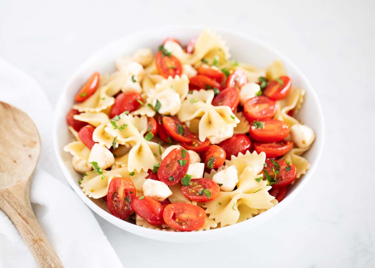 This easy Caprese pasta salad is made with a simple combination of the most delicious classic trio! Juicy tomatoes, fresh mozzarella, and basil. Then combined with cooked pasta and tossed together with a light and zesty dressing. Caprese pasta salad in bowl.