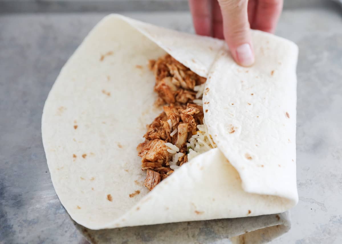 Folding a chicken burrito on a sheet pan. 