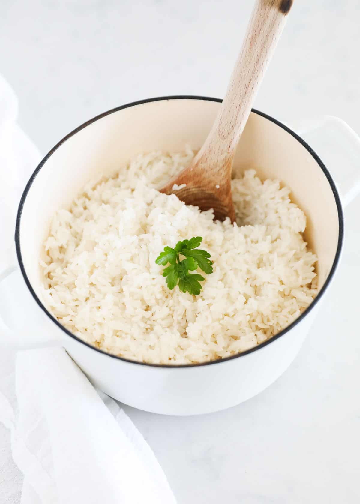 Cooked coconut rice in a white pot with wooden spoon.
