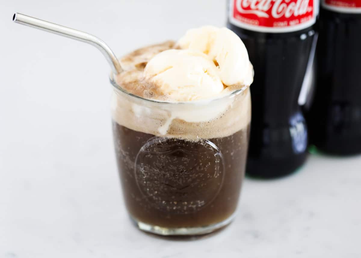 Coke float in glass cup with a straw.
