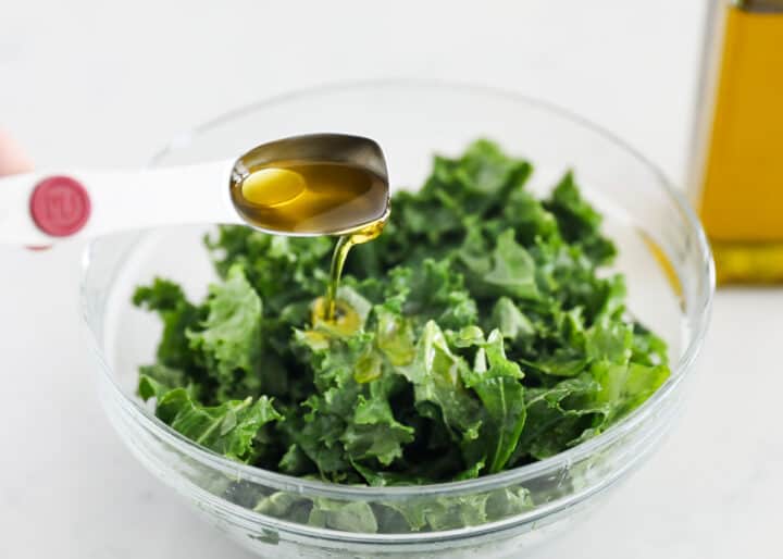 pouring oil over kale in bowl 