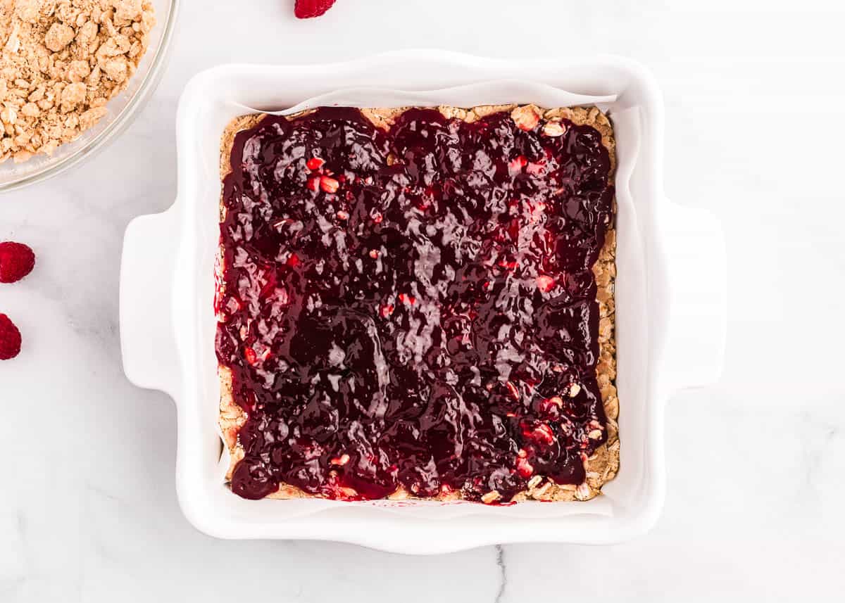 Chewy raspberry crumble bars made with a buttery oatmeal base, fresh raspberry jam and then finished off with a sprinkle more of the oatmeal crumb topping. You only need 7 ingredients and 15 minutes of prep time to make this easy summer dessert! Raspberry crumb bars in white pan.