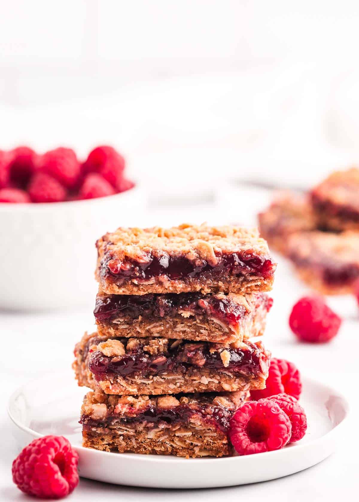 Chewy raspberry crumble bars made with a buttery oatmeal base, fresh raspberry jam and then finished off with a sprinkle more of the oatmeal crumb topping. You only need 7 ingredients and 15 minutes of prep time to make this easy summer dessert! Raspberry crumb bars on white plate.