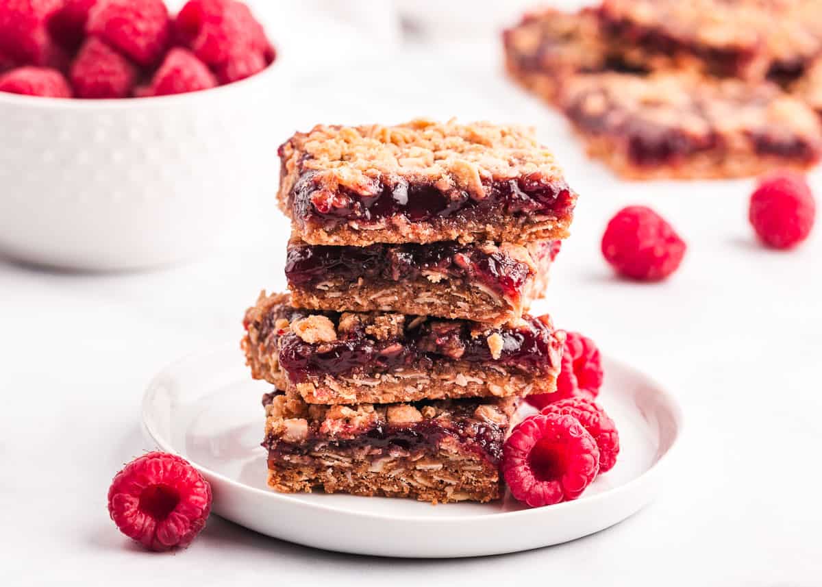 Chewy raspberry crumble bars made with a buttery oatmeal base, fresh raspberry jam and then finished off with a sprinkle more of the oatmeal crumb topping. You only need 7 ingredients and 15 minutes of prep time to make this easy summer dessert! Raspberry crumb bars on white plate.