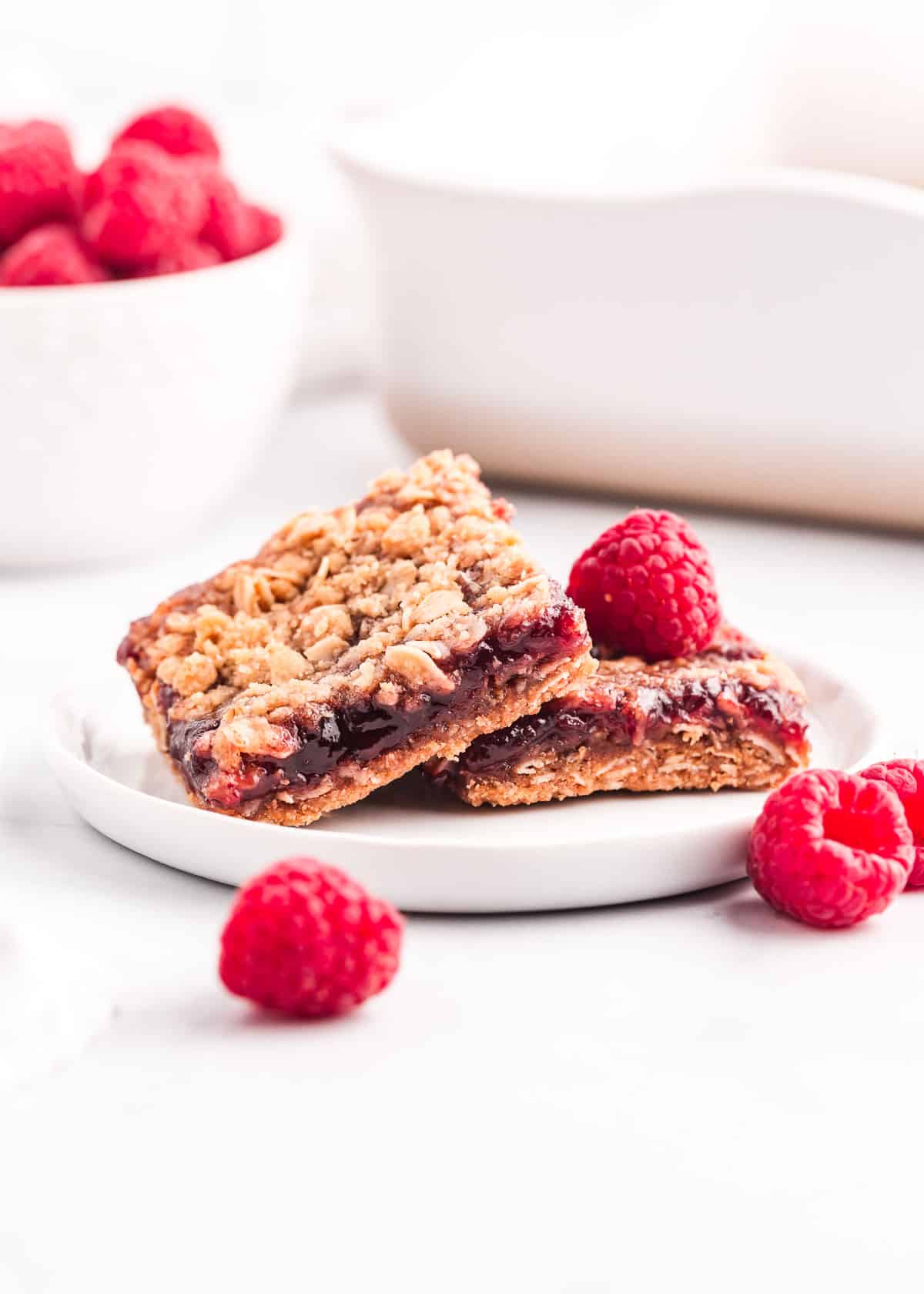 Chewy raspberry crumble bars made with a buttery oatmeal base, fresh raspberry jam and then finished off with a sprinkle more of the oatmeal crumb topping. You only need 7 ingredients and 15 minutes of prep time to make this easy summer dessert! Raspberry crumb bars on white plate.
