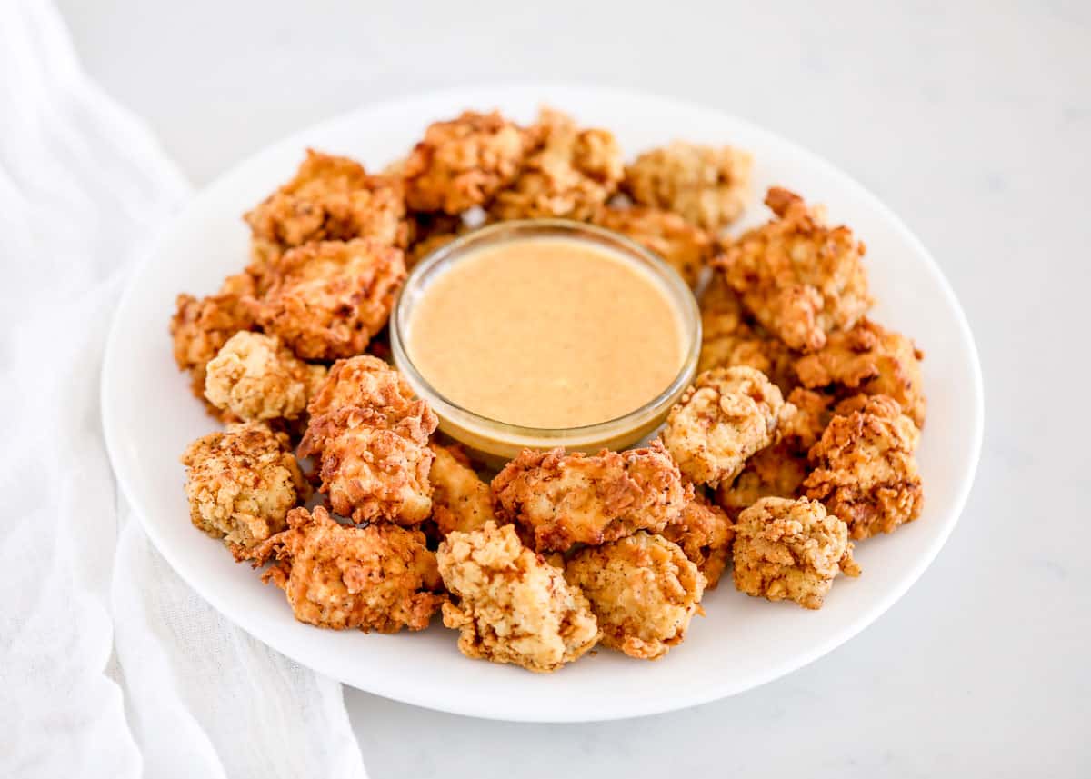 This Chick-fil-A nuggets recipe is a spot-on copycat version of the original. Complete with the signature flavors of a deliciously seasoned crispy coating tender bites of juicy chicken. Serve hot with your favorite dipping sauces! Chick fil a nuggets on white plate with sauce.