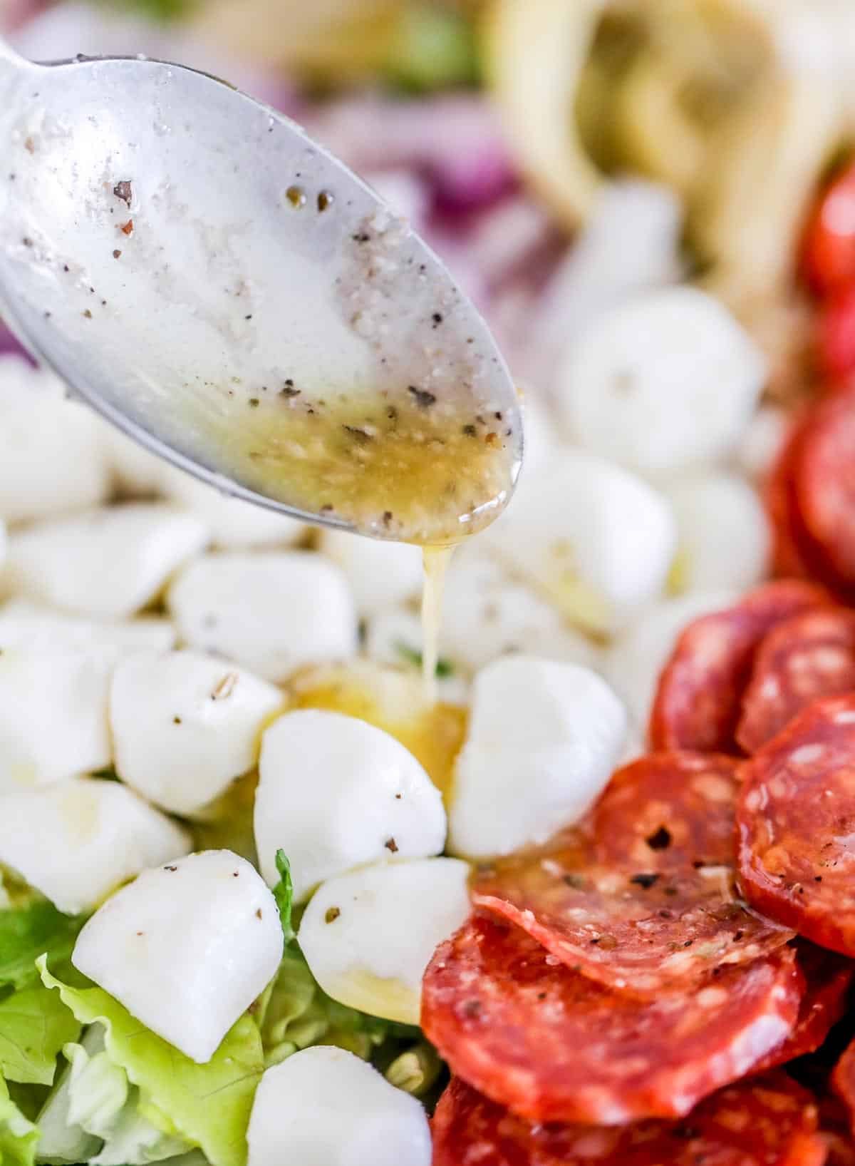 Drizzling Italian dressing on salad with spoon.