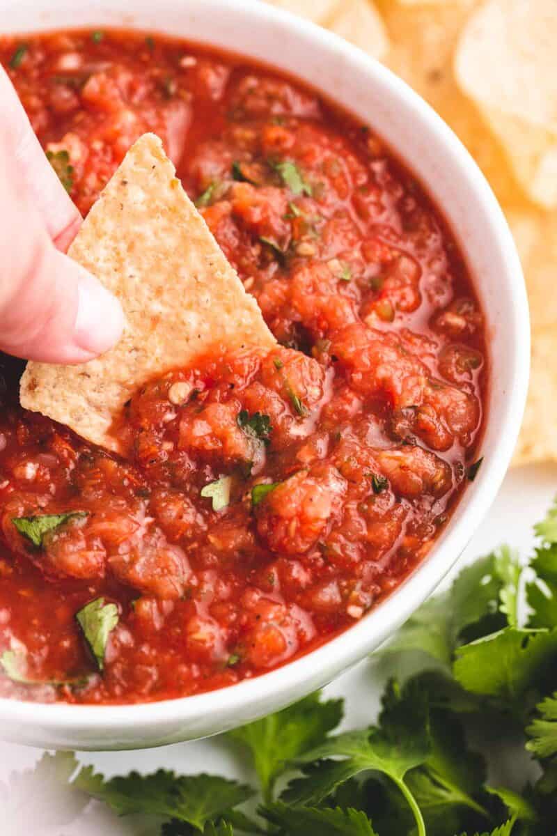 dipping a chip into a bowl of salsa