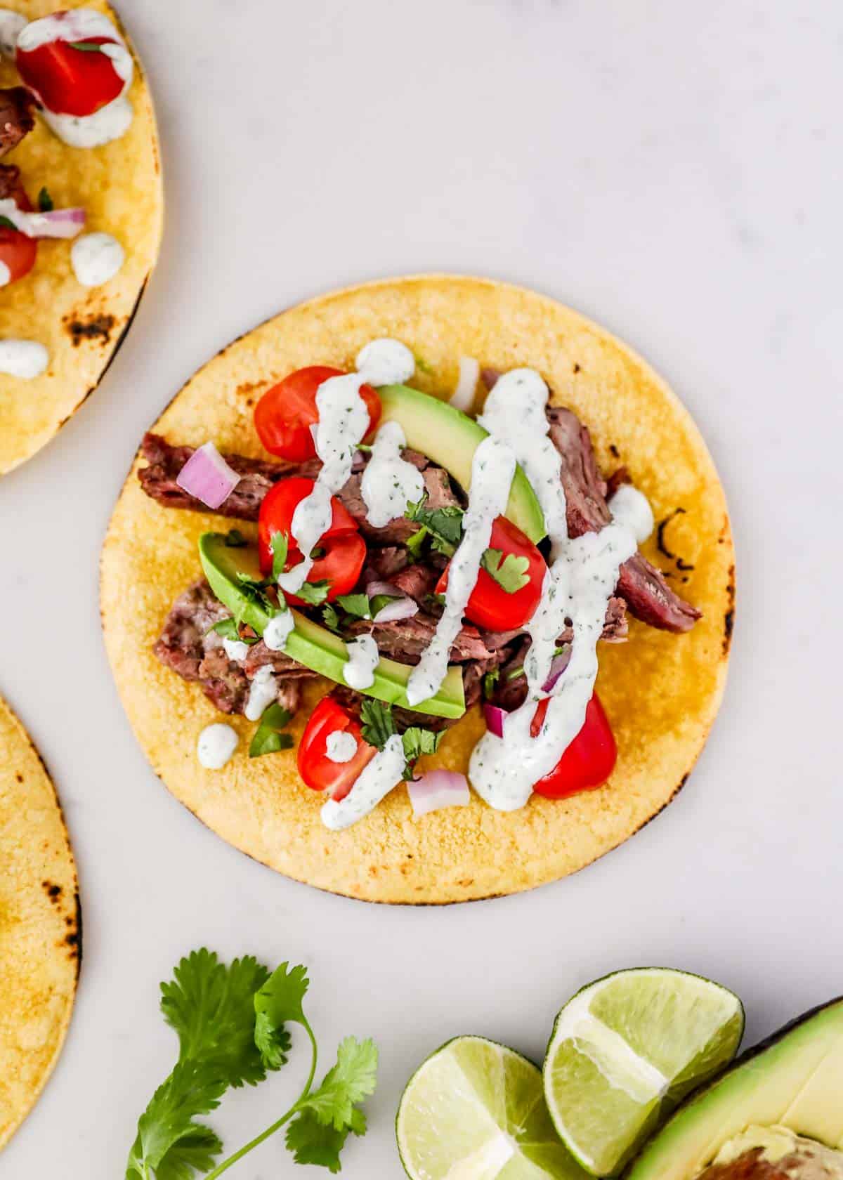 These skirt steak tacos are an explosion of bold flavors and the perfect way to enjoy tender slices of marinated steak. No more chasing the taco trucks, now you can make the ultimate Mexican street food at home! Skirt steak taco with lime and cilantro.