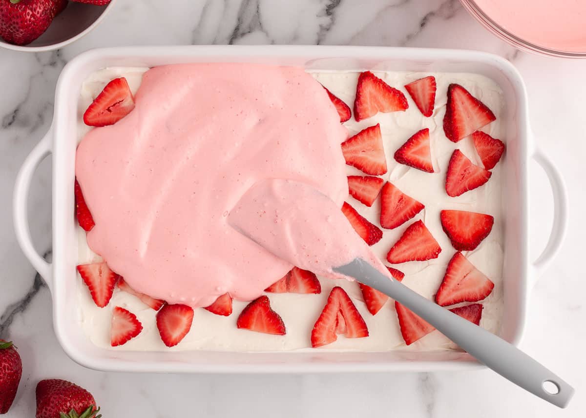 Spreading jello mixture over strawberries.