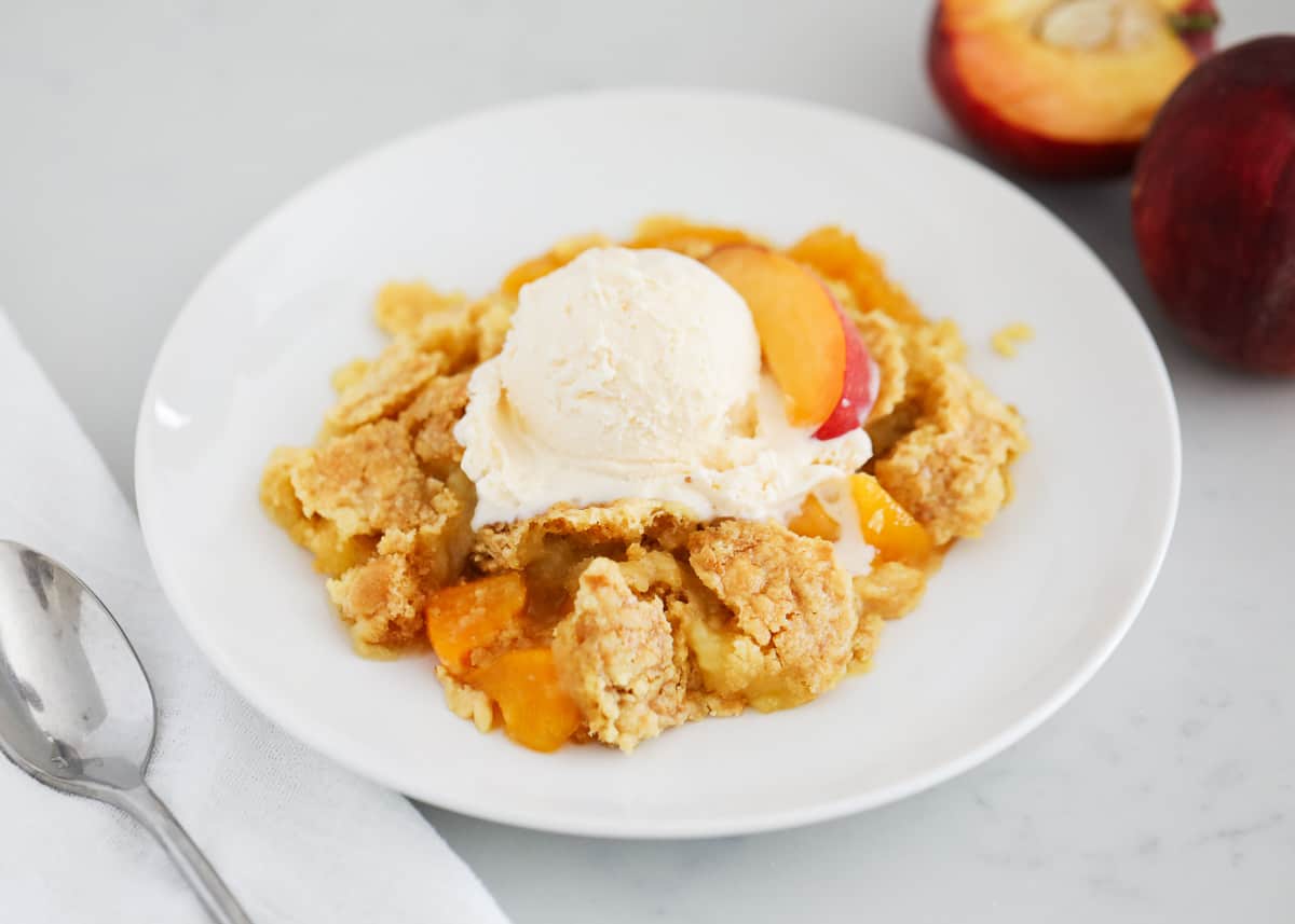 Peach dump cake and ice cream on white plate.