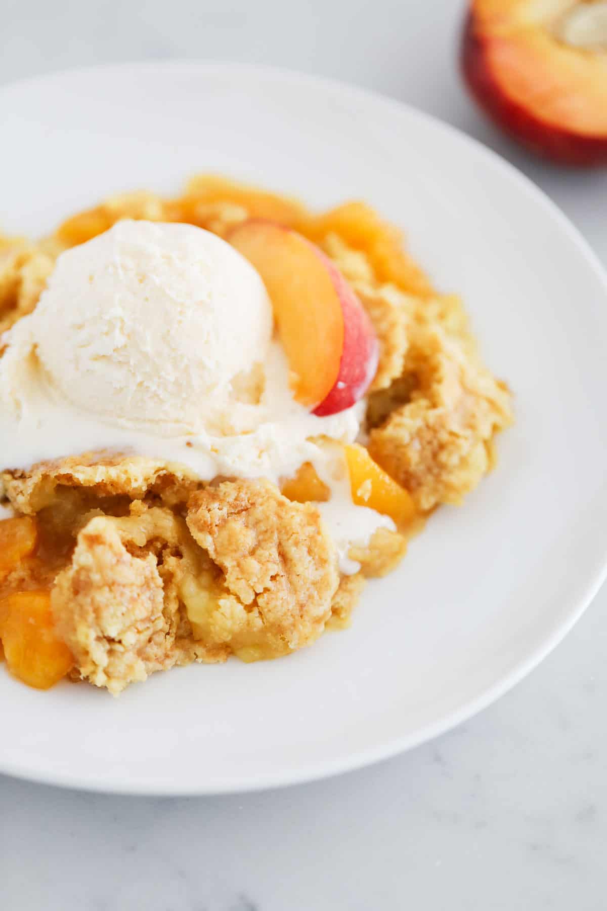 Peach dump cake and ice cream on white plate.