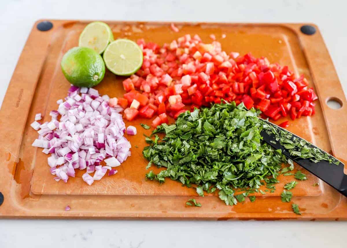 Cilantro, red onion, lime, tomatoes on cutting board for black bean salsa.